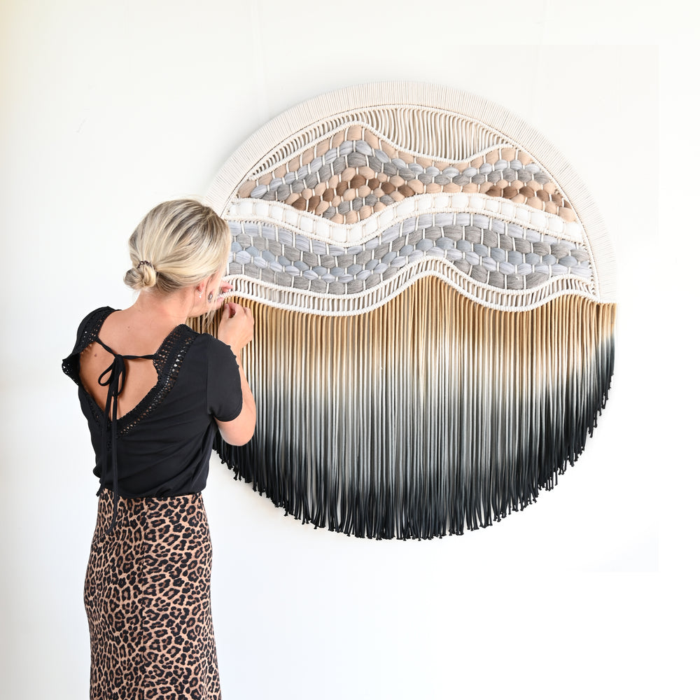 large circular wall art piece with wavy design and fringe.